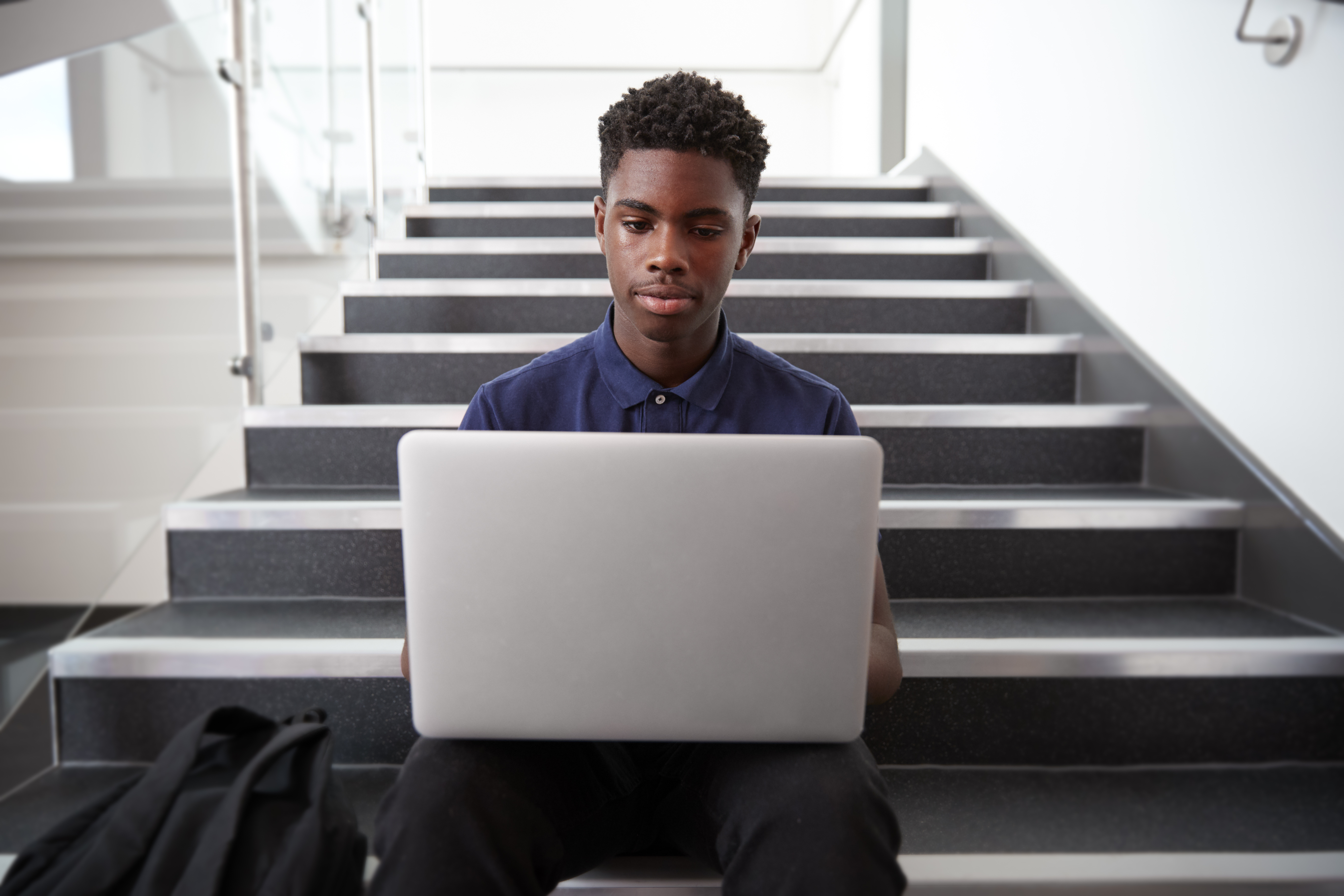 Male Student Sitting On Staircase And Using Laptop