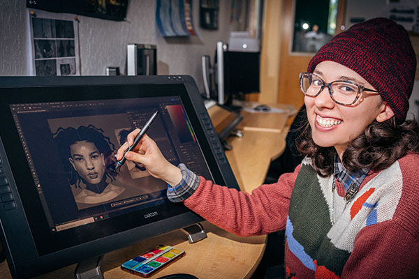 USV Digital Art & Animation student drawing a portrait on a Wacom tablet monitor and smiling.